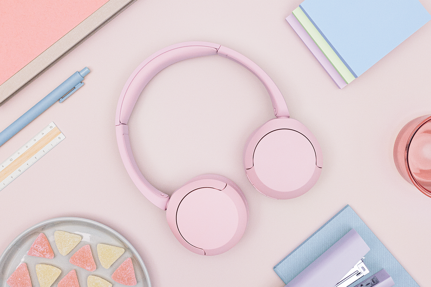 A pair of pink Sony WH-CH520 headphones on a pastel desk.
